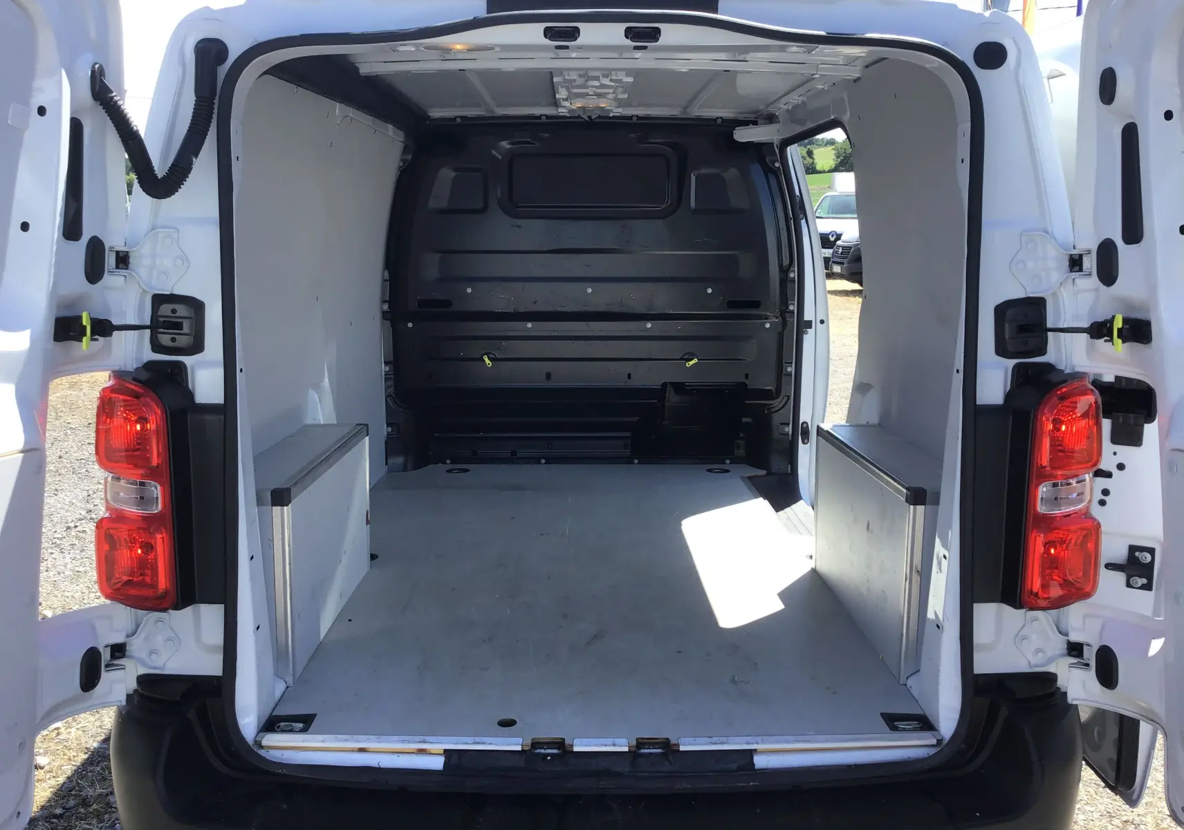 Vue arrière ouverte du fourgon blanc Opel Vivaro M 1.5 BlueHDi 120 2023, montrant l'espace de chargement vide et aménagé.