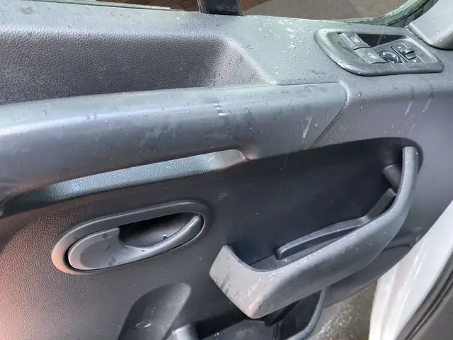 Gros plan sur la poignée intérieure noire de la porte côté conducteur du Renault Master blanc, avec commandes de vitres électriques.