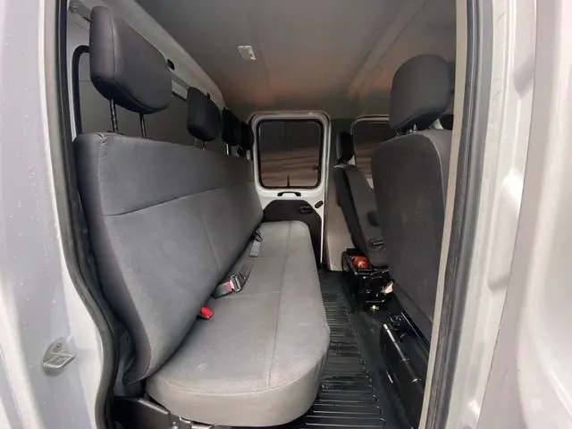 Vue intérieure côté droit du double cabine Renault Master blanc, montrant la banquette arrière en tissu noir et les sièges avant.