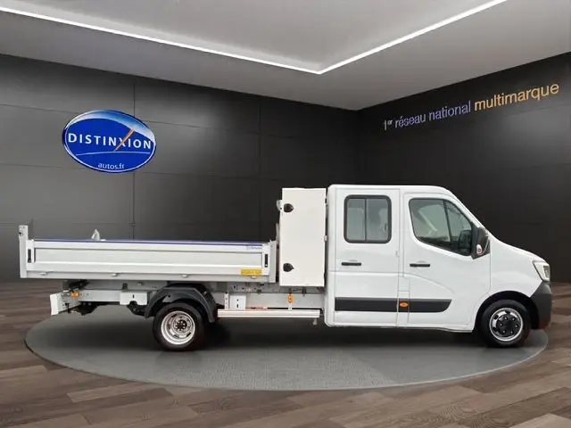 Vue de profil côté droit d'un Renault Master blanc double cabine avec benne et coffre, en intérieur showroom.