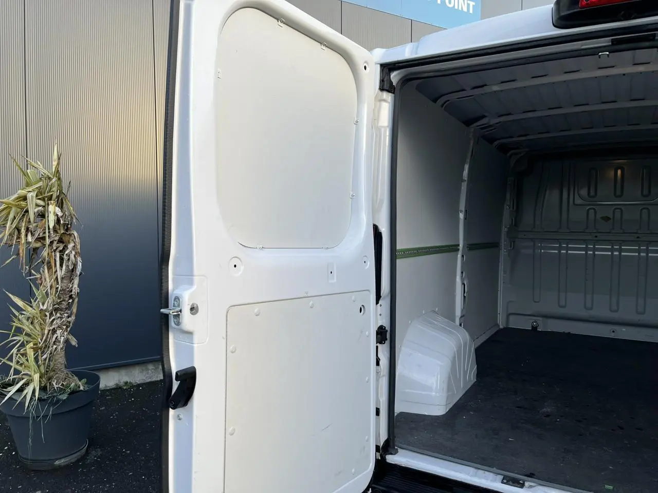 Vue partielle intérieure montrant la porte arrière gauche ouverte du fourgon blanc Opel Movano 2024 avec espace de chargement vide.