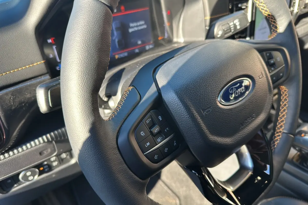 Gros plan sur le volant cuir noir avec surpiqûres marron du Ford Ranger 2025, montrant les commandes multifonctions.