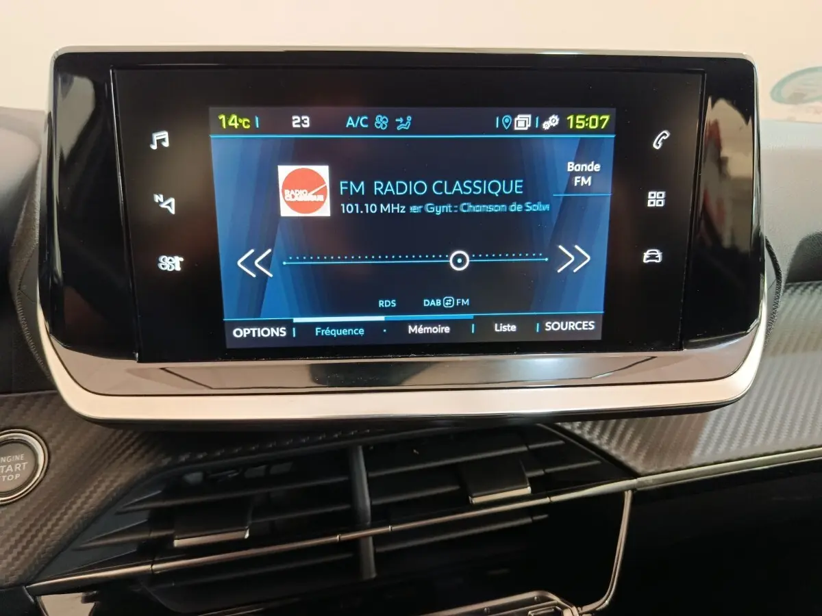 Écran tactile central de la Peugeot 208 électrique Active Business R 2022, affichant une radio FM sur tableau de bord noir.
