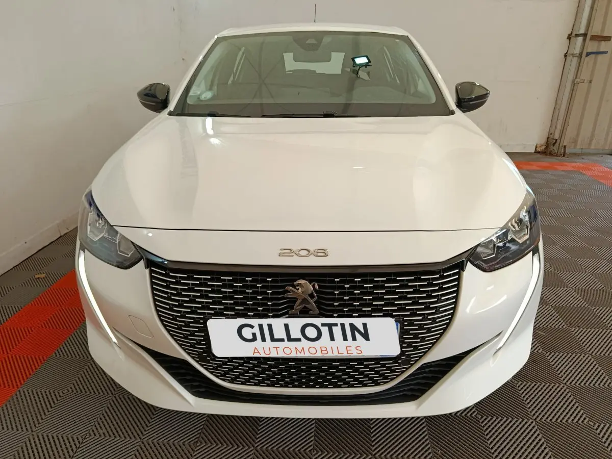 Vue avant d'une Peugeot 208 électrique blanche, avec calandre noire et feux LED distinctifs allumés.