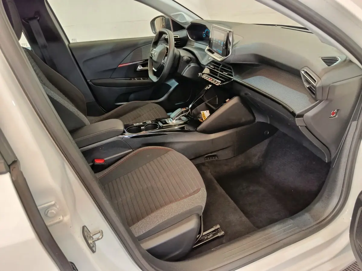 Intérieur avant droit de la Peugeot 208 électrique blanche, avec tableau de bord moderne et écran tactile central.