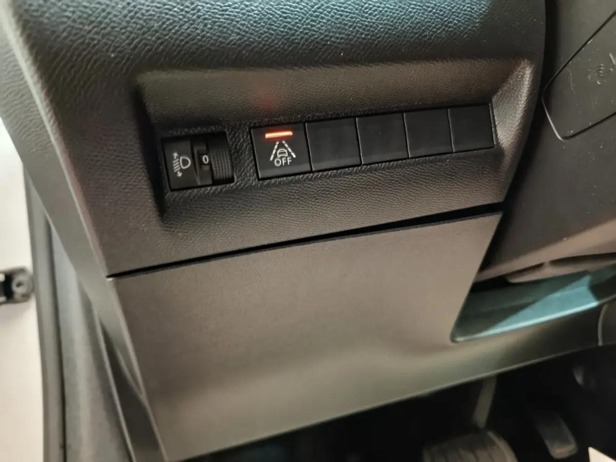 Détail intérieur du tableau de bord côté conducteur de la Peugeot 208 électrique blanche, avec commandes d’éclairage et d’aide à la conduite.