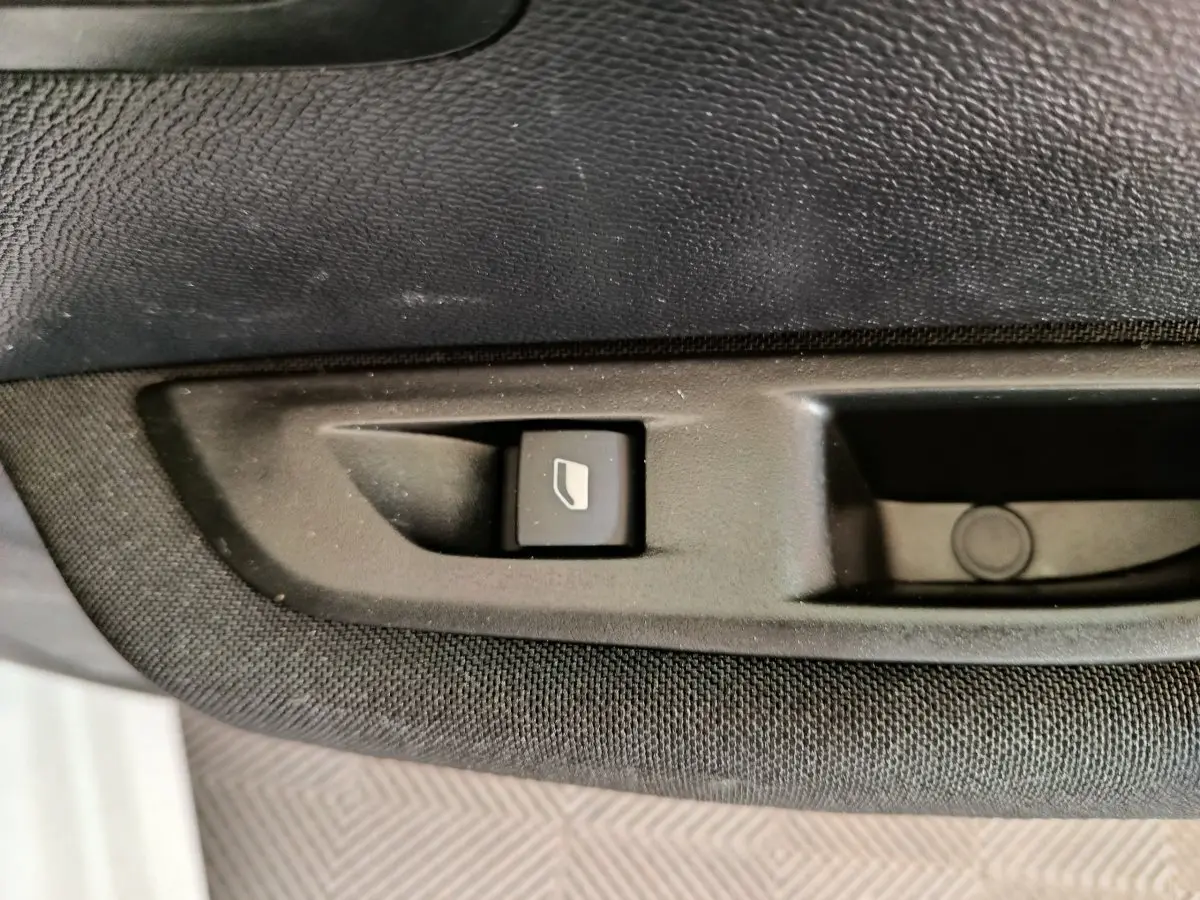 Bouton de commande de lève-vitre sur la porte intérieure noire d'une Peugeot 208 électrique blanche, vue rapprochée.