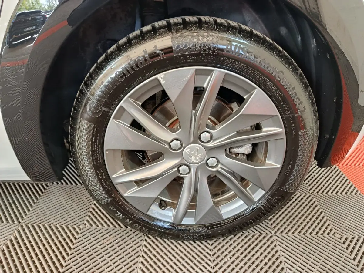 Gros plan sur la roue avant droite de la Peugeot 208 électrique blanche, avec jante alliage et pneu Continental.