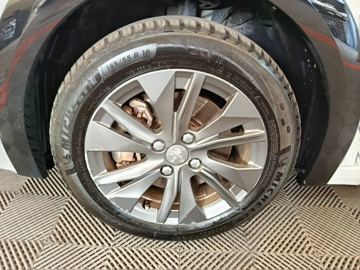 Gros plan sur la roue avant droite d'une Peugeot 208 électrique blanche, jante alliage avec logo Peugeot central.