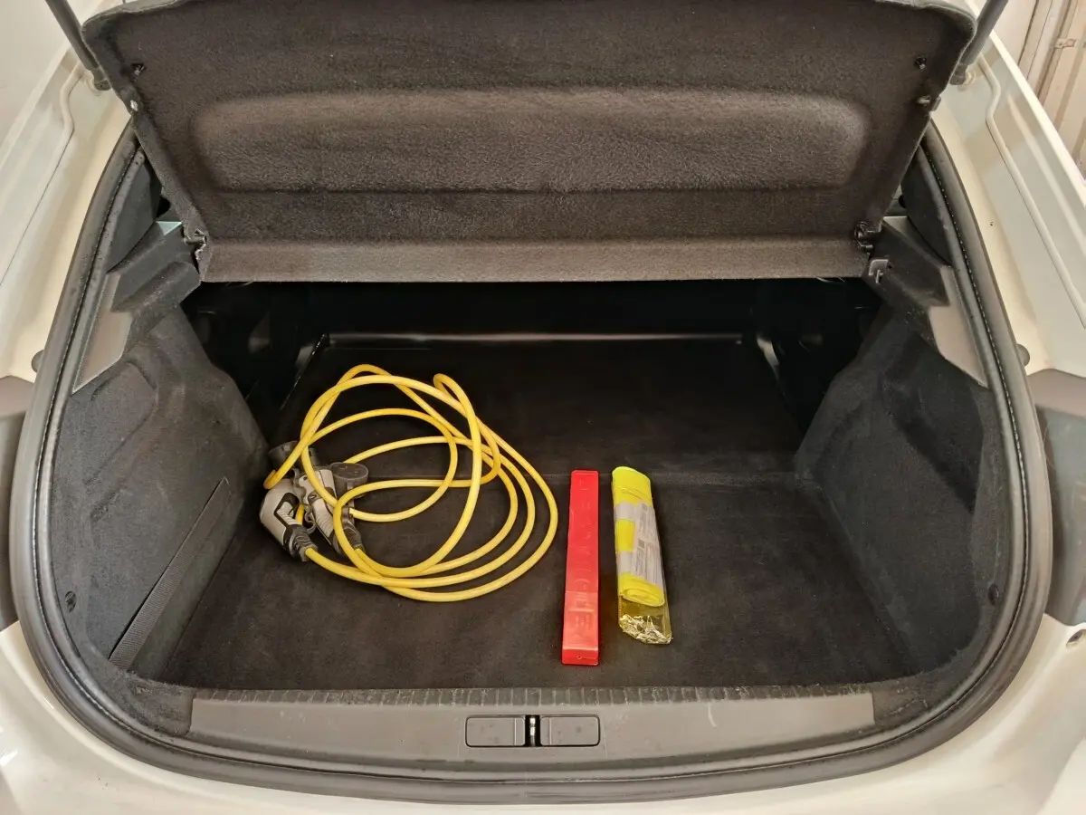 Coffre ouvert d’une Peugeot 208 électrique blanche, montrant un câble de recharge jaune et un triangle de signalisation rouge.