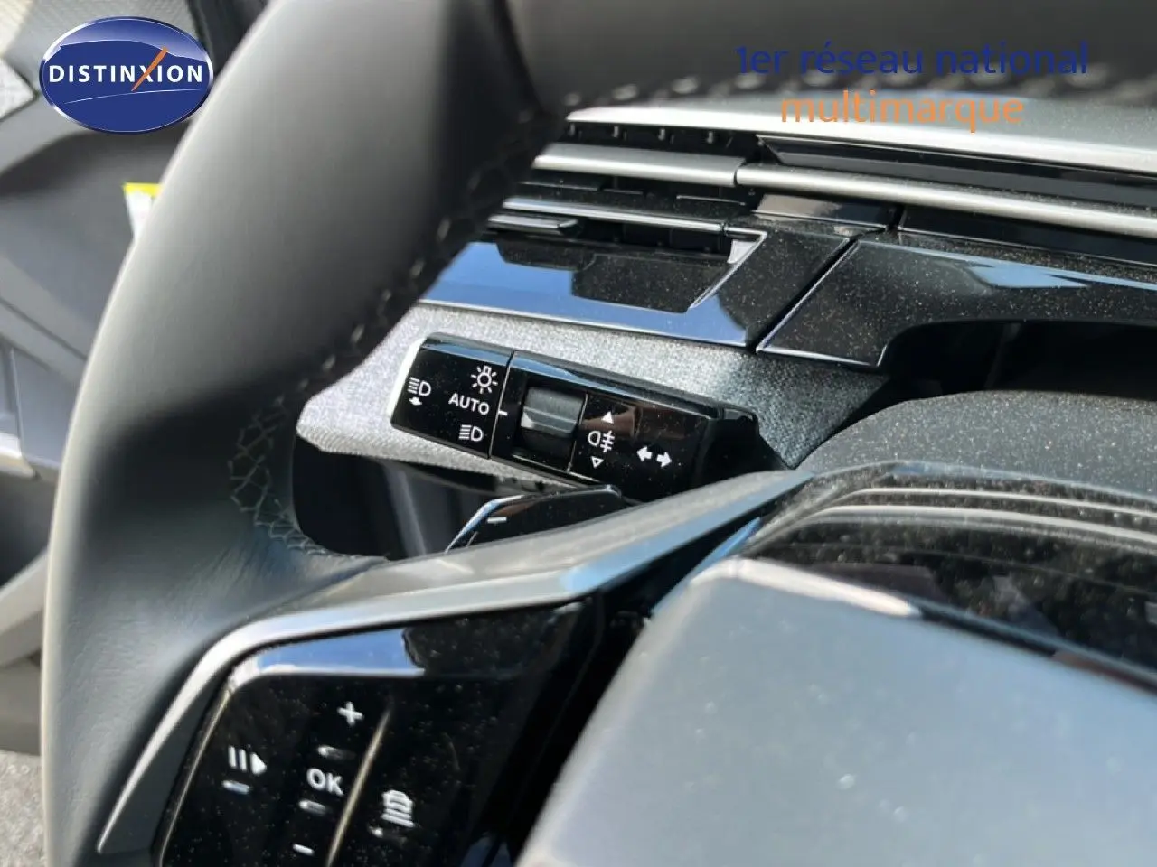 Gros plan sur le volant noir et la commande des phares du Peugeot 5008 gris Artense, intérieur moderne et épuré.