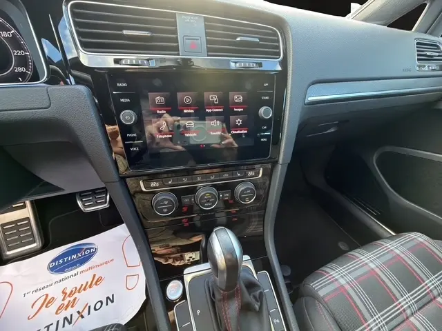 Vue intérieure centrée sur la console centrale d'une Volkswagen Golf GTI Performance blanche, avec écran tactile et levier de vitesse.