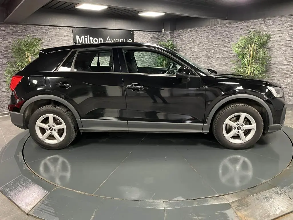 Audi Q2 noir vue de profil côté gauche, avec jantes aluminium 5 branches dans un showroom intérieur.