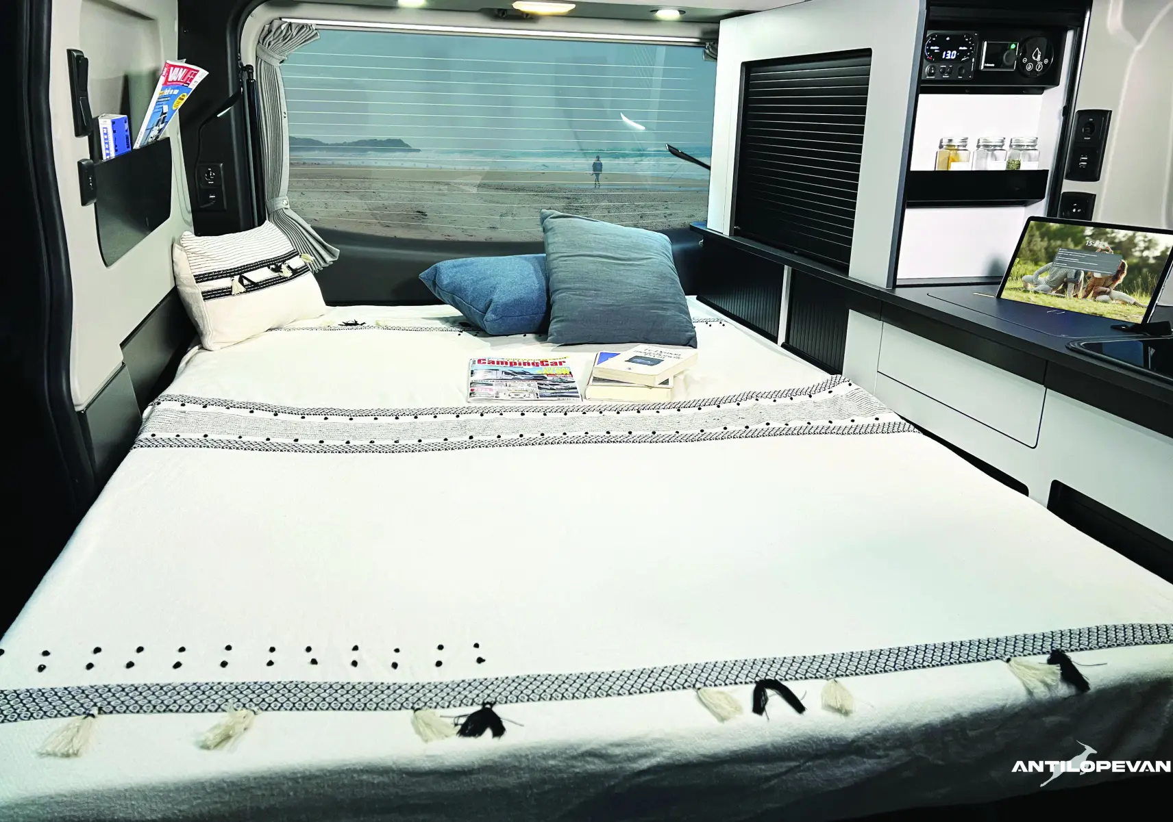 Vue intérieure arrière du van aménagé Renault Trafic blanc glacier, montrant le lit avec coussins et rangements intégrés.