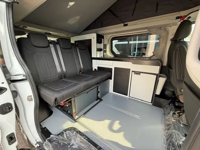 Intérieur côté gauche du Renault Trafic Fourgon blanc glacier 2025, banquette noire 3 places et meubles de cuisine intégrés.