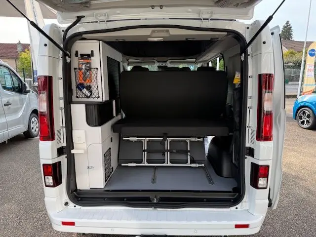Vue arrière du Renault Trafic Fourgon blanc glacier avec portes ouvertes montrant l'aménagement intérieur et banquette rabattue.