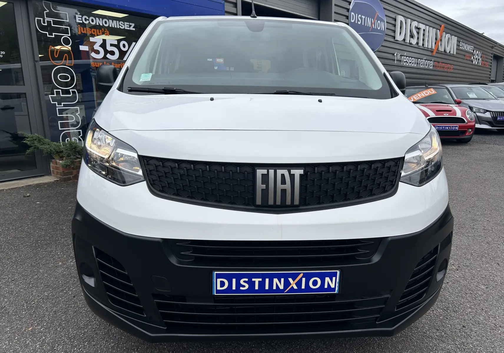 Vue frontale d'un FIAT Scudo Combi blanc avec calandre noire et logo FIAT bien visible, stationné devant un concessionnaire.