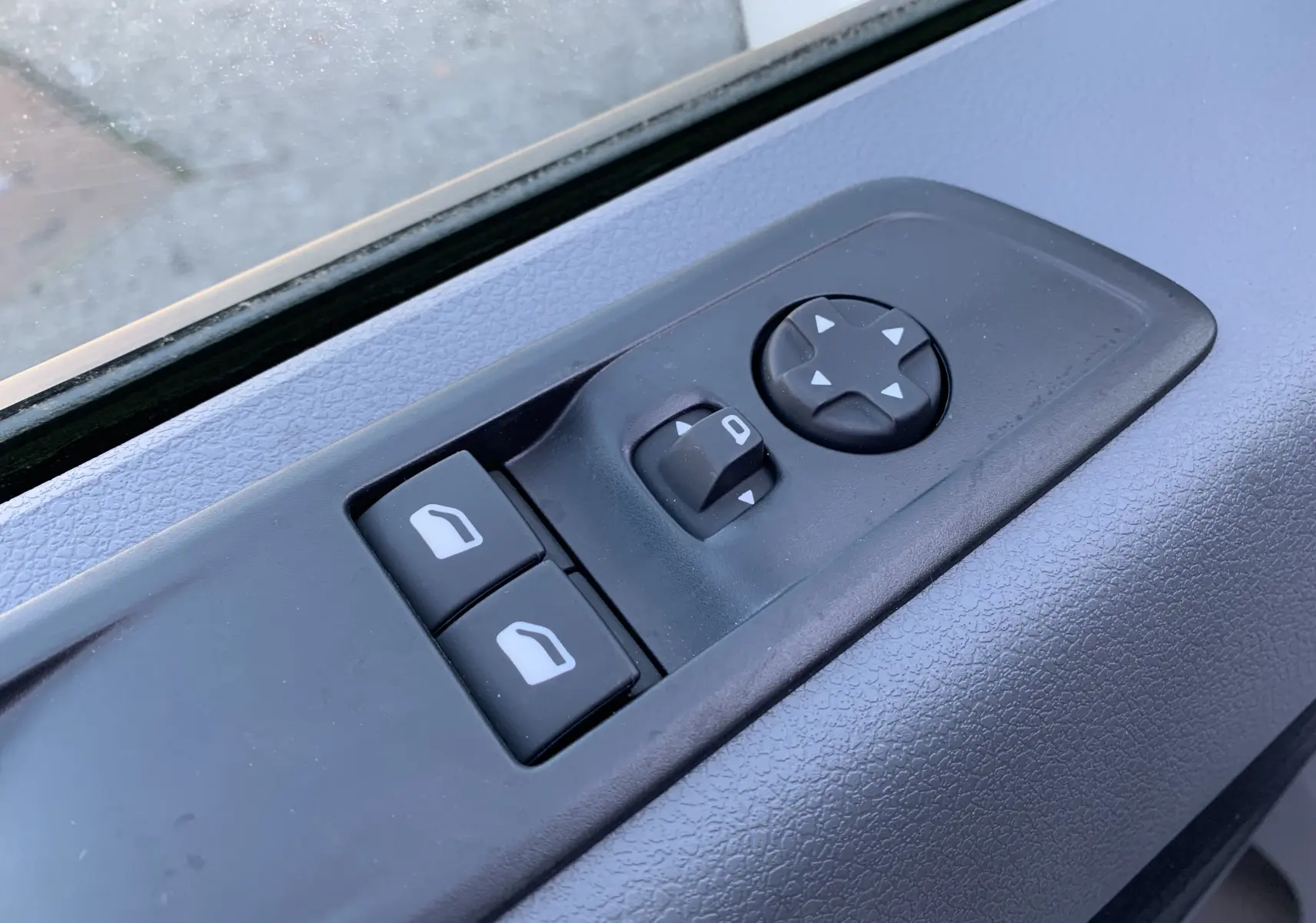 Gros plan sur les commandes de lève-vitres et réglage des rétroviseurs côté gauche du Fiat Scudo Combi blanc électrique 2022.