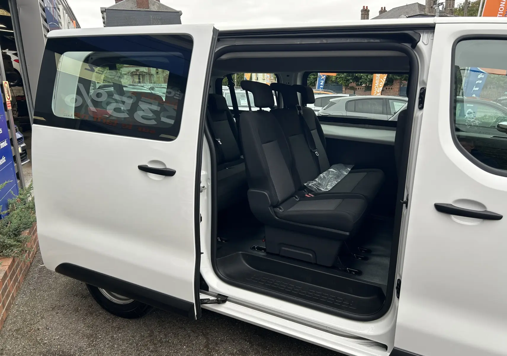 Vue latérale gauche d'un FIAT Scudo Combi blanc avec porte coulissante ouverte révélant trois sièges passagers noirs.