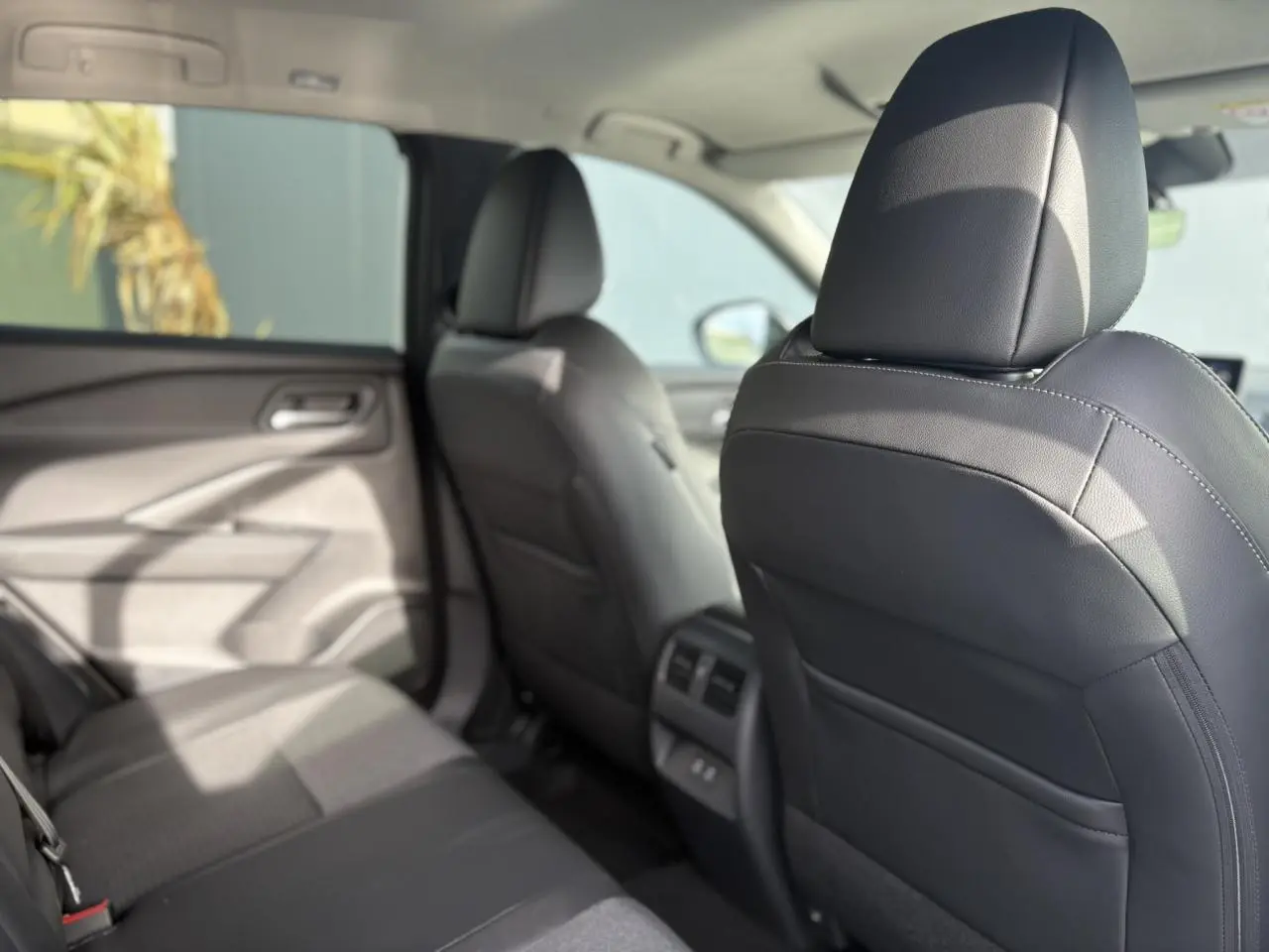 Vue intérieure arrière côté gauche du Nissan Qashqai blanc nacré 2025, montrant les sièges noirs et les aérateurs centraux.