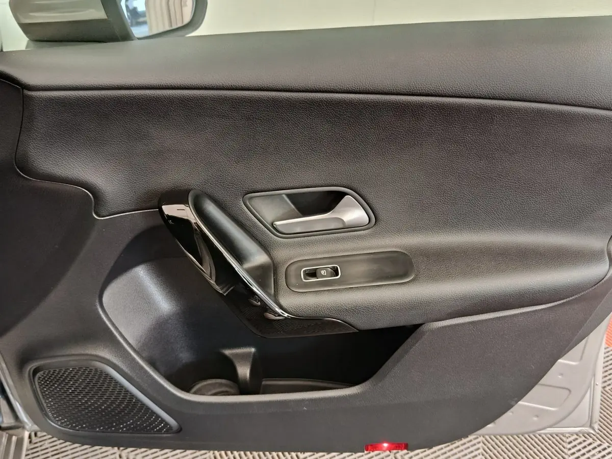 Vue intérieure du panneau de porte côté gauche noir de la Mercedes Classe A 180 Business Line 2020 avec poignée argentée et commande de fenêtre.