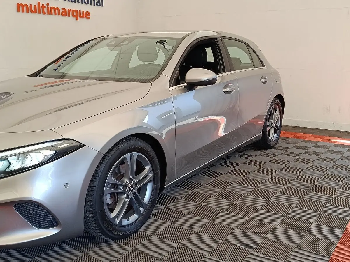 Vue 3/4 avant droit d'une Mercedes Classe A 180 Business Line gris clair, avec jantes alliage et phares LED allumés.