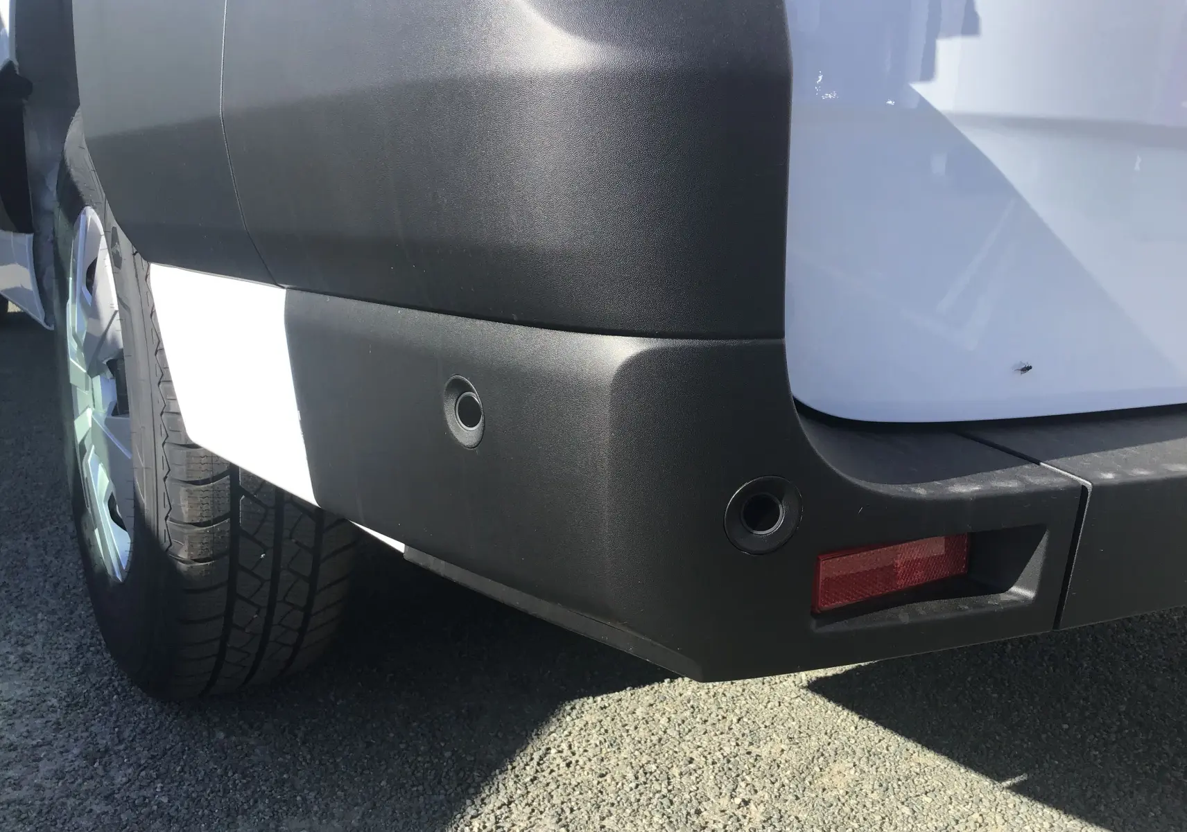 Gros plan sur le pare-chocs arrière droit blanc du Renault Master 2025 avec capteurs de recul et feu rouge intégré.