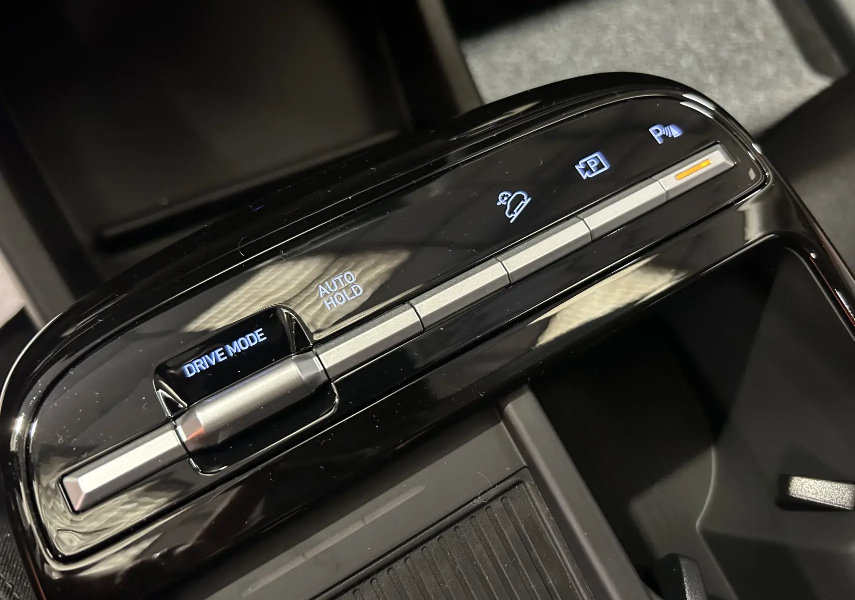 Gros plan sur la console centrale noire brillante du Hyundai Tucson IV Ph.2 STYLE avec commandes Drive Mode et Auto Hold éclairées.