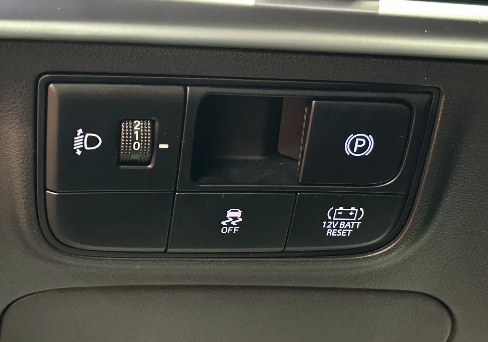 Gros plan sur les commandes de réglage des phares et frein de parking électronique du Hyundai Tucson 2025 intérieur noir.