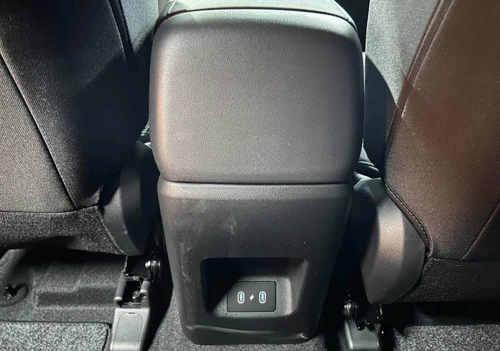 Prise USB arrière entre les sièges noirs du Hyundai Tucson 2025 STYLE hybride en intérieur sombre.