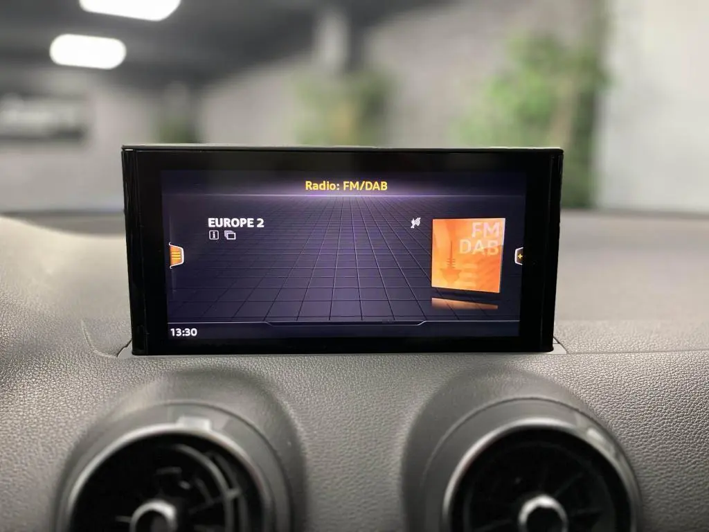Écran central de l'Audi Q2 2022 affichant la radio FM/DAB, avec tableau de bord noir et aérateurs ronds visibles.