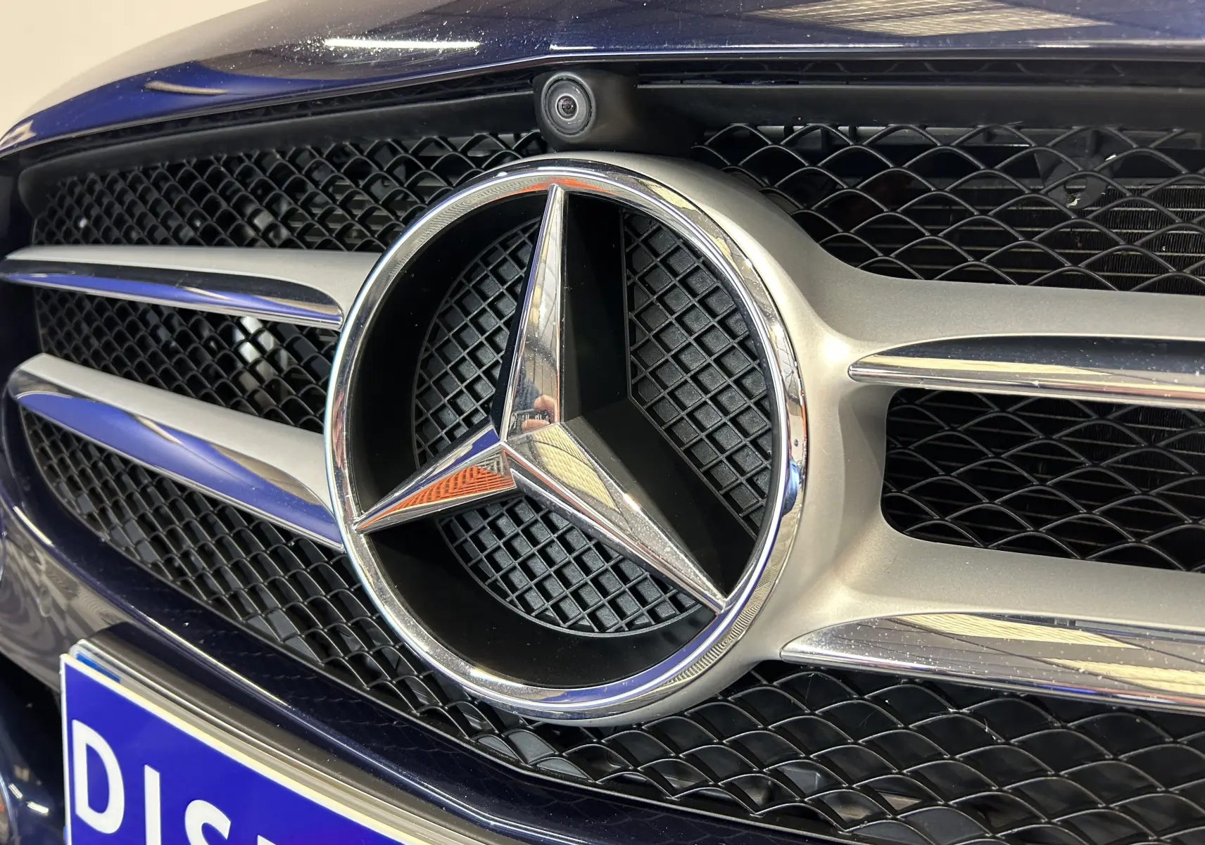 Gros plan sur la calandre bleue d'une Mercedes Classe C 200d avec l'étoile emblématique et caméra 360° intégrée.