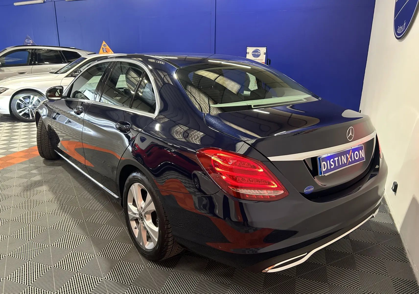 Vue 3/4 arrière droite d'une Mercedes Classe C 200d bleu foncé avec feux arrière allumés en intérieur showroom.