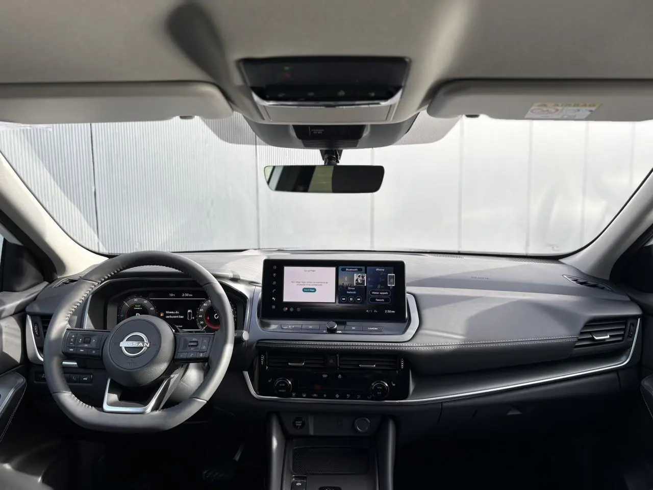 Vue frontale intérieure du Nissan Qashqai blanc nacré 2025, tableau de bord moderne avec écran tactile central et volant cuir.