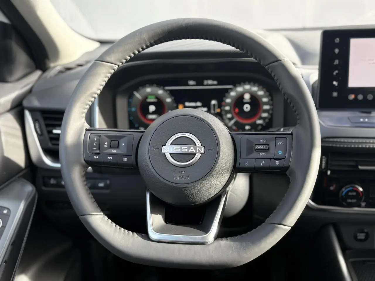 Vue frontale du volant cuir noir du Nissan Qashqai blanc nacré 2025 avec commandes intégrées et tableau de bord numérique.
