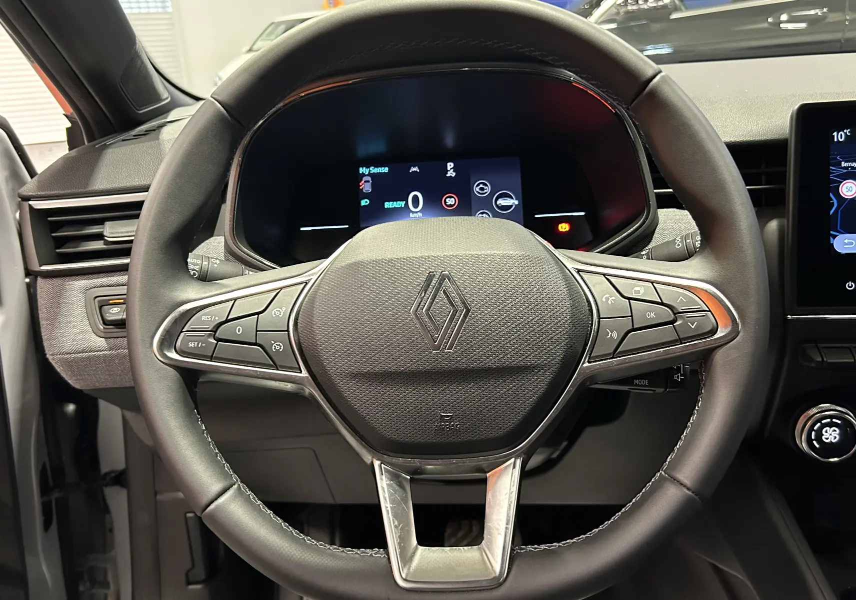 Vue intérieure centrée sur le volant noir de la Renault Clio V E-Tech 145ch avec tableau de bord numérique allumé.