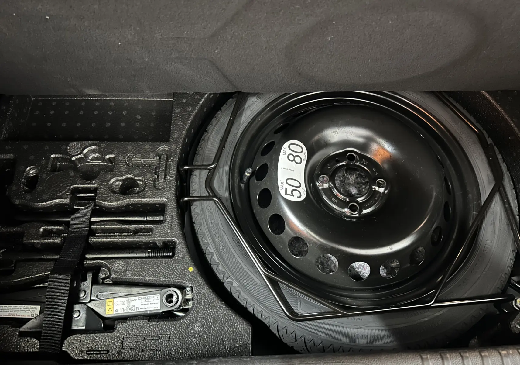 Vue rapprochée du coffre de la Renault Clio V gris Rafale Metal montrant la roue de secours et les outils de dépannage.