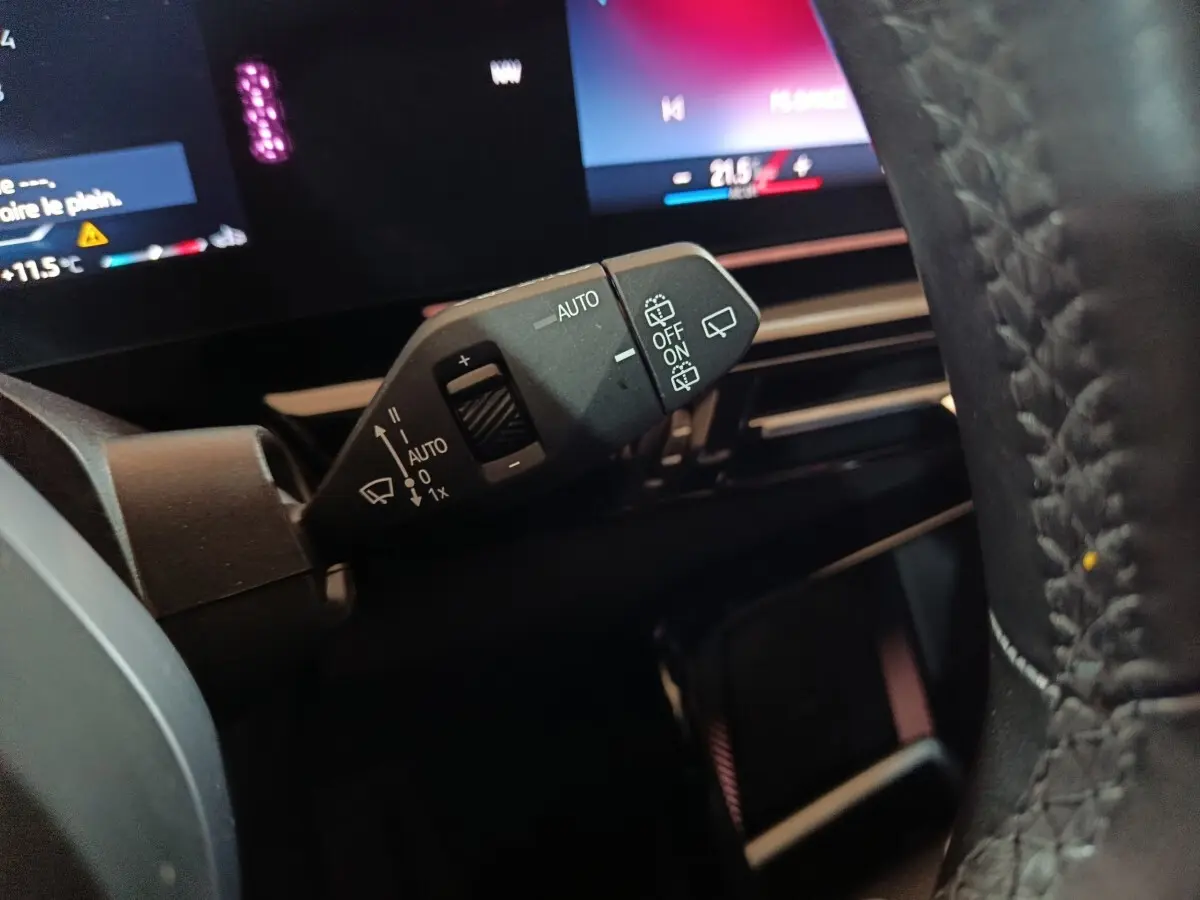 Gros plan sur la commande d’essuie-glace à gauche du volant en cuir d’un BMW X1 noir, tableau de bord digital en arrière-plan.