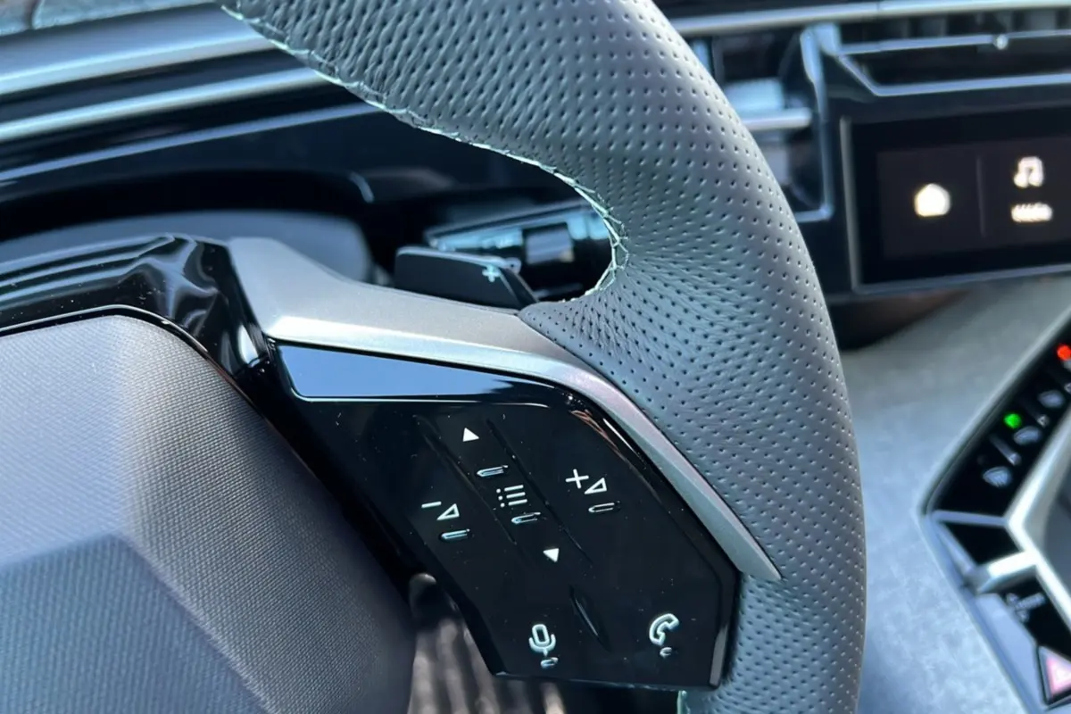Gros plan sur la partie gauche du volant en cuir perforé gris avec commandes tactiles du Peugeot 3008 Hybrid 2025.