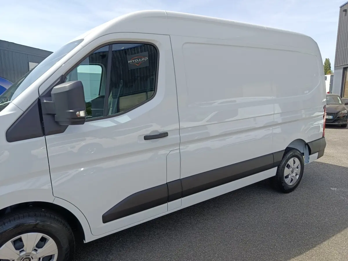 Vue latérale droite d’un utilitaire blanc Renault Master FG L2H2 avec protections noires sur les portières et rétroviseur noir.