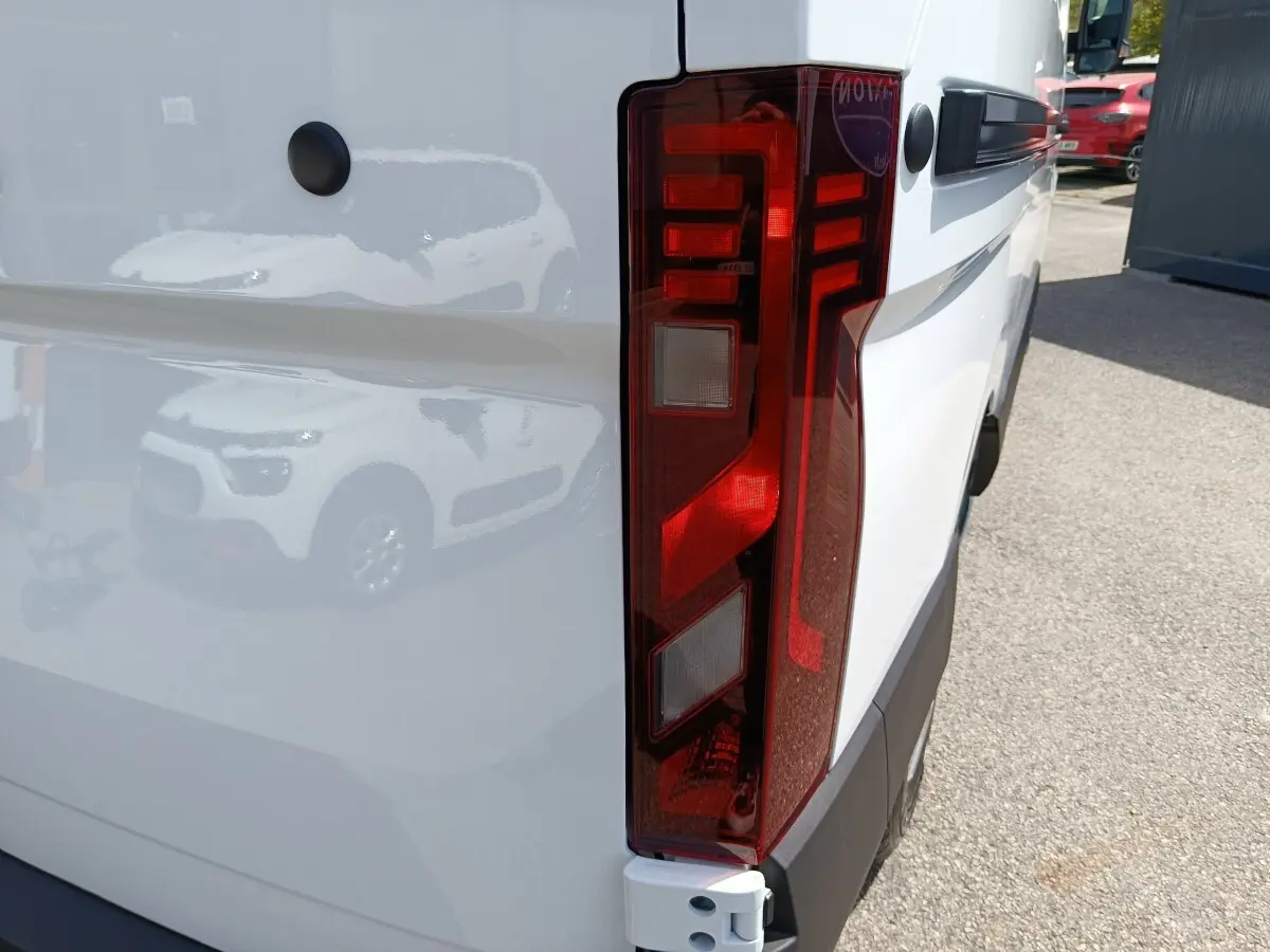 Gros plan sur le feu arrière droit du Renault Master blanc, avec reflet d’un autre véhicule sur la carrosserie.