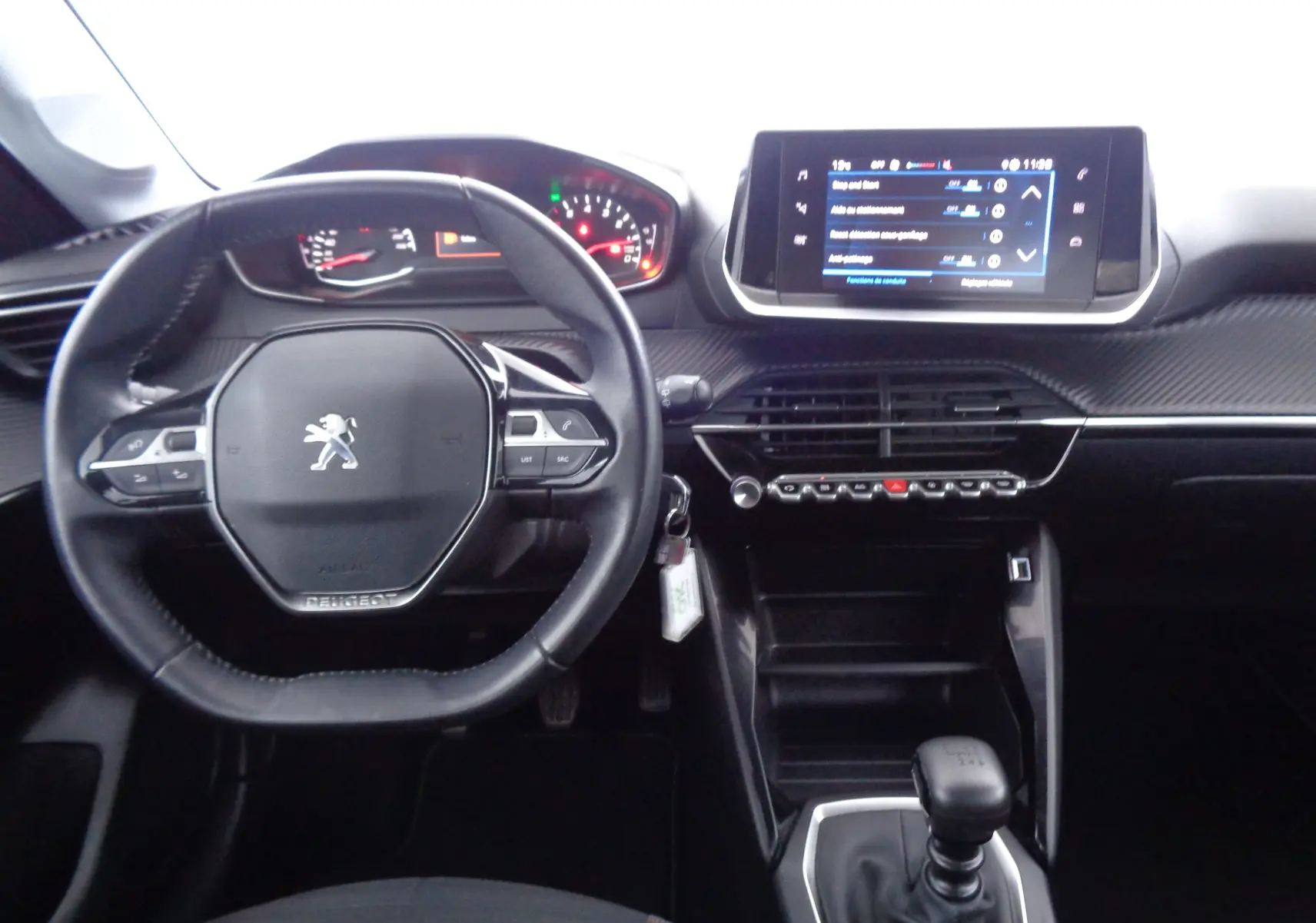 Intérieur de Peugeot 208 rouge Elixir, vue du poste de conduite avec volant compact et écran tactile central.