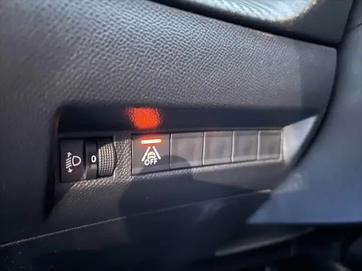 Détail intérieur du tableau de bord montrant les commandes d'éclairage et le témoin d'alerte de sécurité activé sur Peugeot 208 rouge.