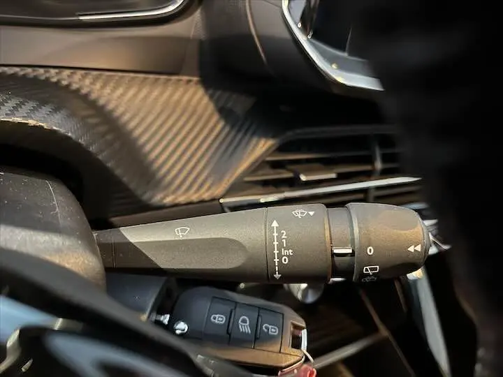 Gros plan sur la commande d'essuie-glace dans l'habitacle d'une Peugeot 208 rouge Elixir Metal, montrant les réglages et la clé.