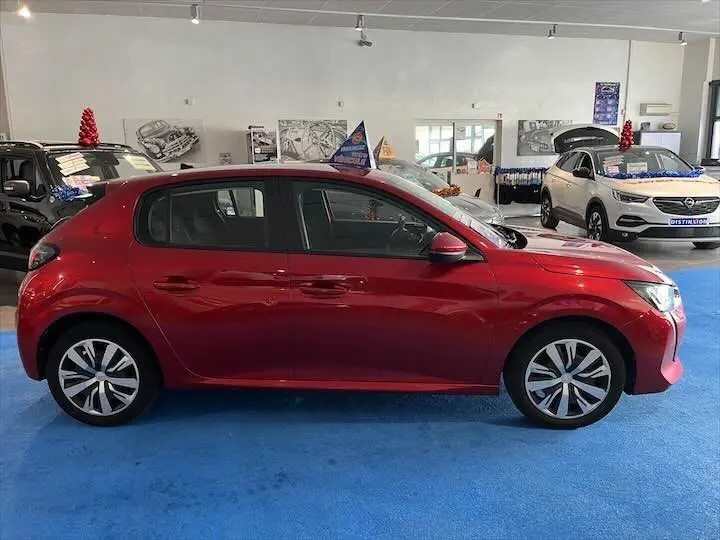 Profil droit d'une Peugeot 208 rouge Elixir Metal exposée en showroom avec jantes alliage et vitres teintées.