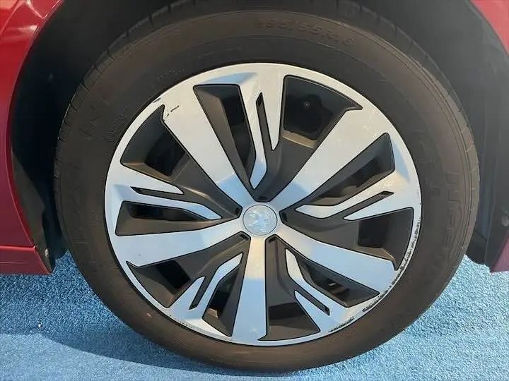 Gros plan sur la roue avant gauche d'une Peugeot 208 rouge Elixir Metal avec jante alliage au design moderne.