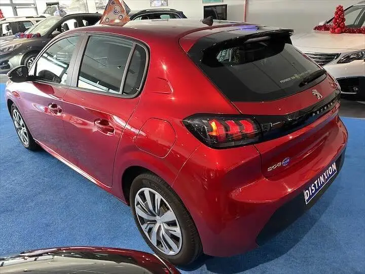 Vue 3/4 arrière droite d'une Peugeot 208 rouge Elixir Metal avec feux arrière allumés en showroom.