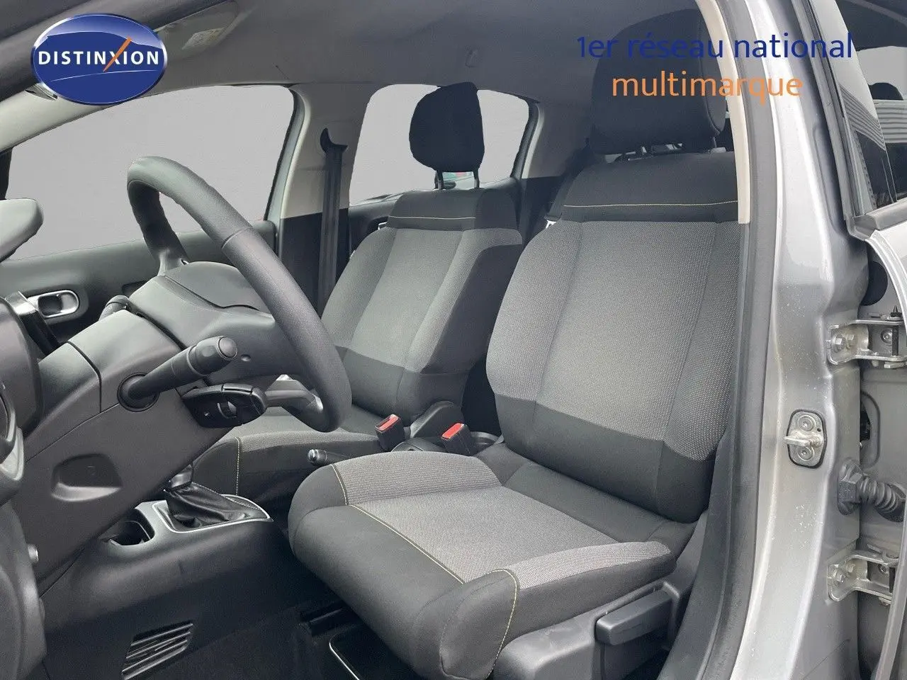 Vue intérieure côté conducteur de la Citroën C3 2023 gris acier, montrant sièges tissu gris et volant noir.