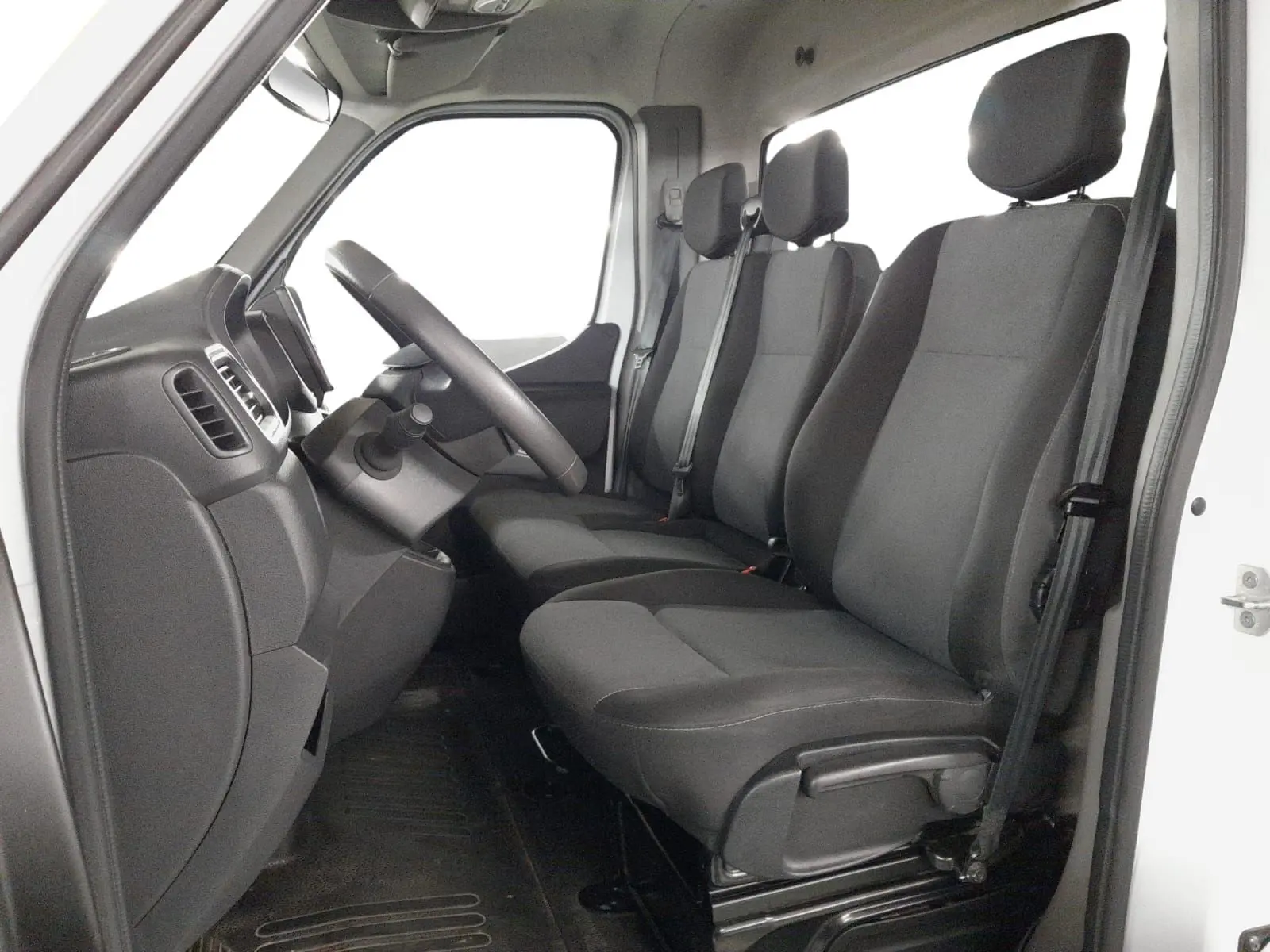 Vue intérieure côté conducteur du Renault Master blanc 2024, montrant les sièges noirs et le tableau de bord simple.