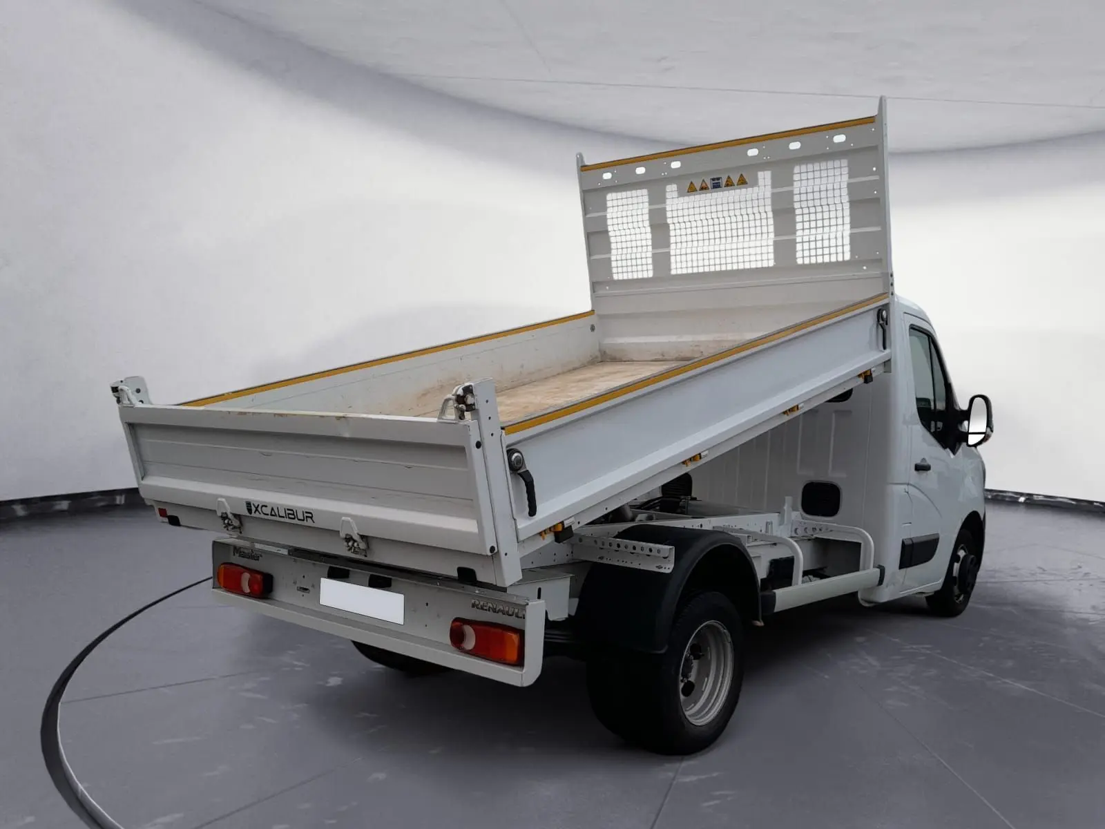 Renault Master blanc vue 3/4 arrière droit avec benne relevée dans un studio lumineux.